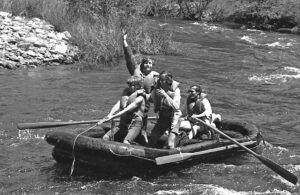 Dick Linford in a raft, hand raised